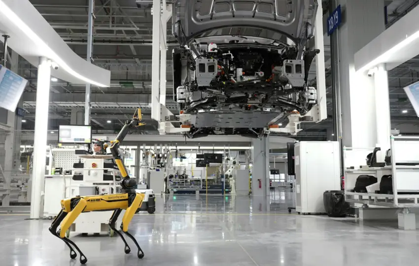 A robotic dog oversees an automated car assembly in a high-tech factory setting.