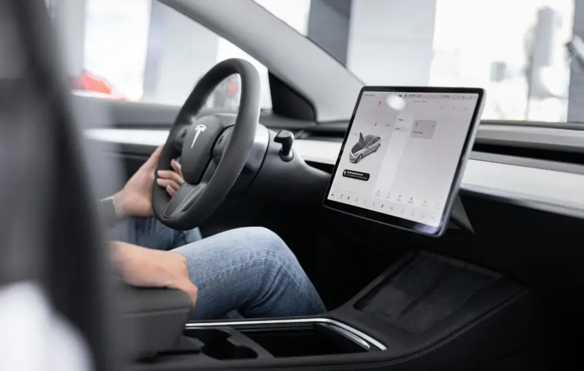 Interior of an electric car showing steering wheel and large touchscreen display, indicating modern technology.